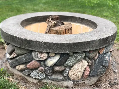 Concrete fire pit with colorful stones in a backyard setting